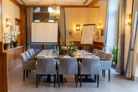 Heller Tagungsraum mit Konferenztischen, Stühlen, Leinwand, Beamer und Flipchart für Meetings und Seminare.