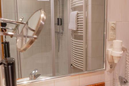 Helles Hotelbadezimmer mit Waschbecken, großem Spiegel, Dusche und Handtuchheizkörper.