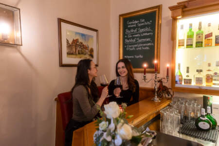 Zwei Frauen genießen ein Glas Rotwein an einer gemütlich beleuchteten Hotelbar.