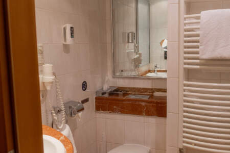 Helles Hotelbadezimmer mit Waschbecken, großem Spiegel, WC und Handtuchheizkörper.