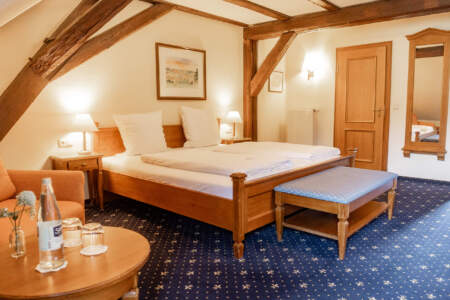 Gemütliches Hotelzimmer mit großem Doppelbett, sichtbaren Holzbalken, Sitzecke und klassischer Holzeinrichtung.