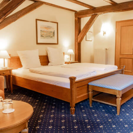 Gemütliches Hotelzimmer mit großem Doppelbett, sichtbaren Holzbalken, Sitzecke und klassischer Holzeinrichtung.
