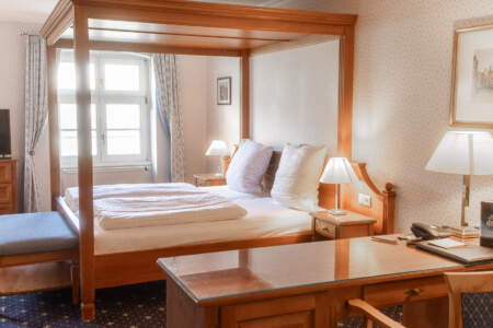 Gemütliches Hotelzimmer mit großem Holzhimmelbett, Schreibtisch, Sitzbereich und klassischer Einrichtung.
