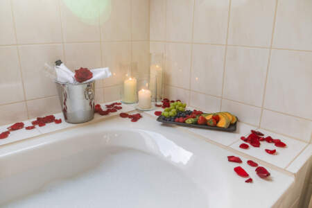 Badewanne mit Schaumbad, Rosenblättern, Kerzen, frischem Obst und gekühltem Getränk.